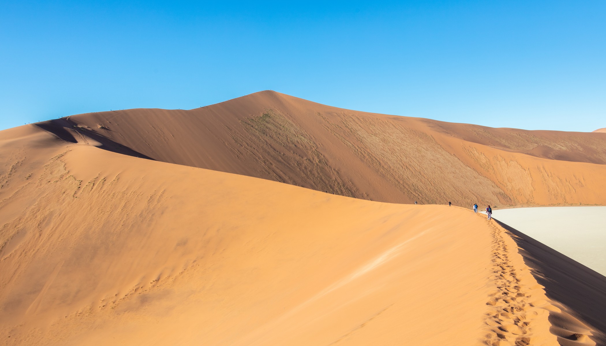 Red Sossusvlei dune ridges and wind-rippled sand beneath a blue Namib sky.