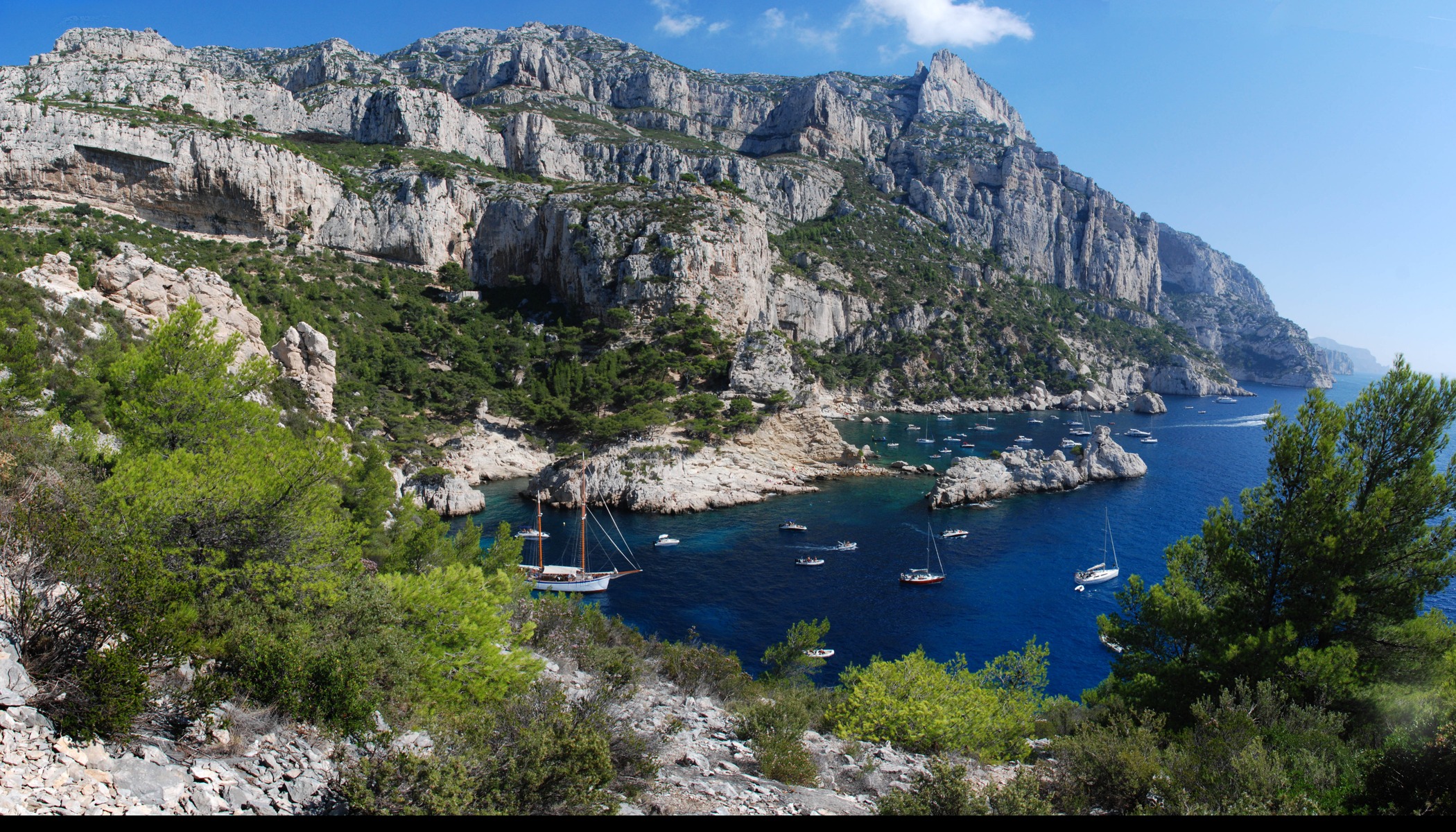 Wide view across the turquoise water, white limestone coves and pine-covered hills of Calanque de Sugiton near Marseille, France.