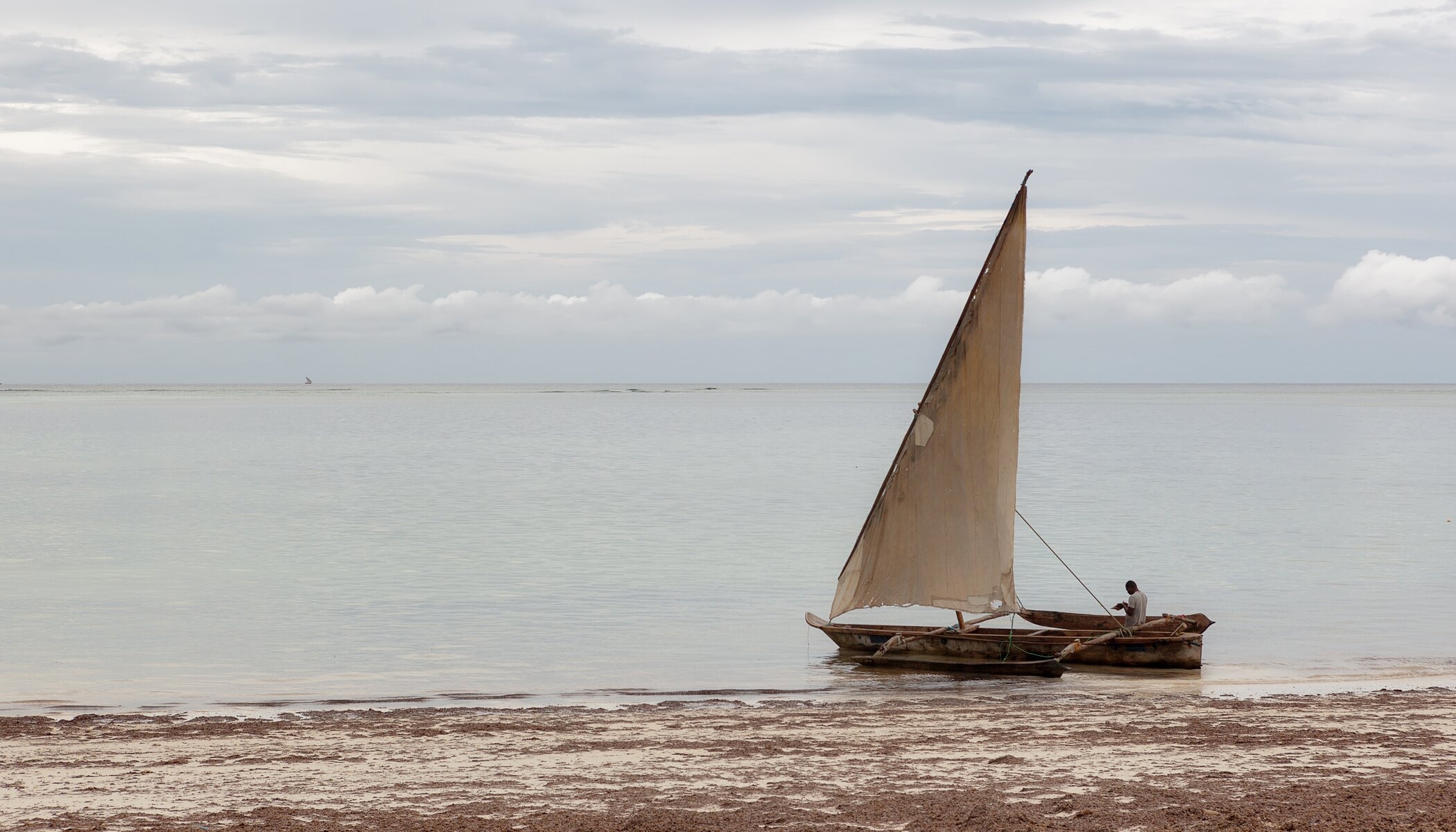 Traditional wooden dhow sailboat on calm Indian Ocean water off a white-sand Zanzibar beach in Tanzania